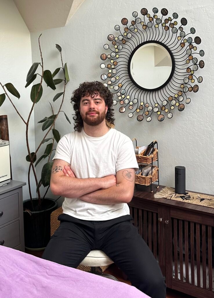 Ezra sitting down next to massage table in their studio